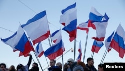 Spectators watch the action standing next to Russian and Crimean flags during celebrations marking the first anniversary of Russia's annexation of Ukraine's Black Sea peninsula of Crimea, in central Simferopol, March 16, 2015. 
