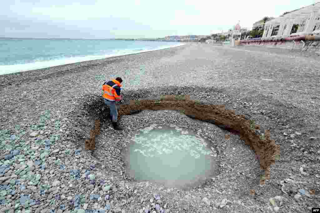 People looks at a two-meter-deep and five-meter-wide crater, filled with brackish water, which has formed on the beach of Lido on the French riviera city of Nice.