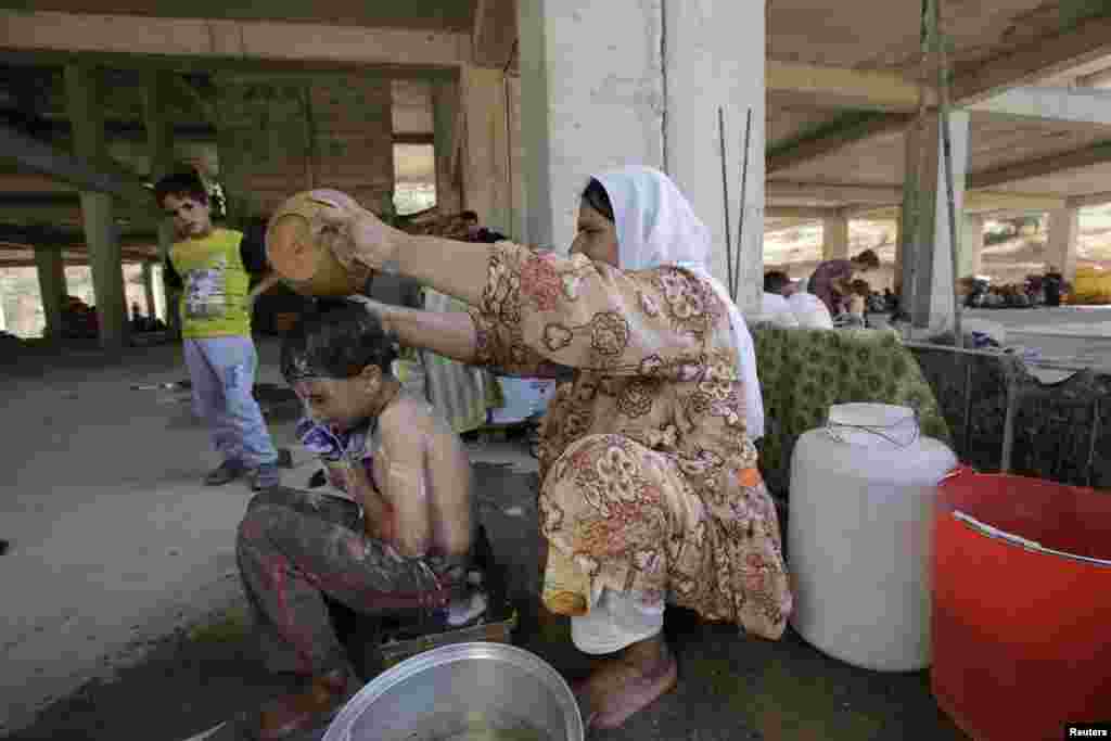 A woman from the minority religious Yazidi sect, who fled the violence in the Iraqi town of Sinjar, cleans her child in an abandoned building which is now used as a shelter for her family and many other regufees, outside the city of Dohuk, Aug. 14, 2014.