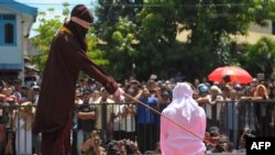 FILE - A religious officer canes an Acehnese youth onstage as punishment for dating outside marriage, which is against Sharia, or Islamic law, outside a mosque in Banda Aceh, Aug. 1, 2016. Aceh's landscape is dotted with Saudi influence, but its religious climate is decidedly not.