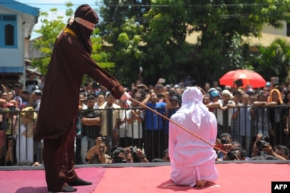 Seorang petugas agama mencambuk seorang pemuda Aceh di atas panggung sebagai hukuman karena berkencan di luar nikah, yang bertentangan dengan Syariah, atau hukum Islam, di luar sebuah masjid di Banda Aceh, 1 Agustus 2016. (Foto: AFP)