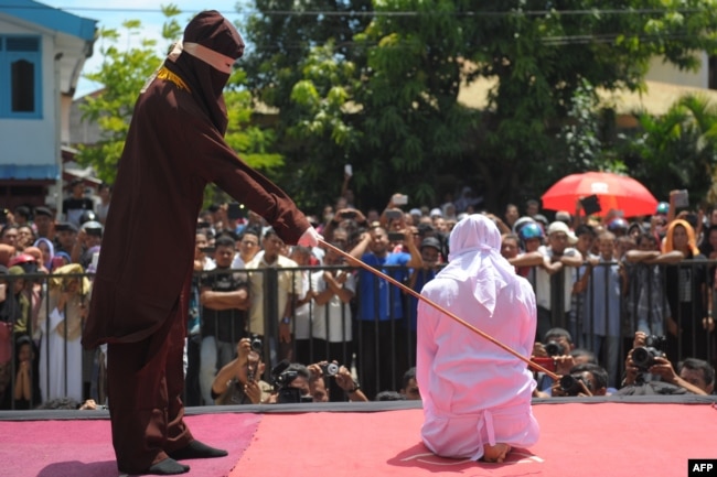 A religious officer canes an Acehnese youth onstage as punishment for dating outside marriage, which is against Sharia, or Islamic law, outside a mosque in Banda Aceh, Aug. 1, 2016. The strictly Muslim province, Aceh has become increasingly conservative in recent years and is the only one in Indonesia implementing Sharia.