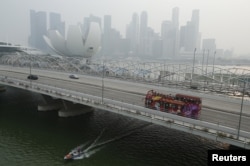 Sebuah bus wisata melewati kawasan pusat bisnis yang diselimuti kabut di Singapura pada 29 September 2015. (Foto: Reuters)