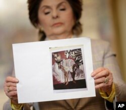 During a news conference in New York, Feb. 21, 2019, attorney Gloria Allred holds up a picture of Latresa Scaff, left, and Rochelle Washington, posing in front of a picture of R. Kelly, on the night they say they became victims of his sexual advances.