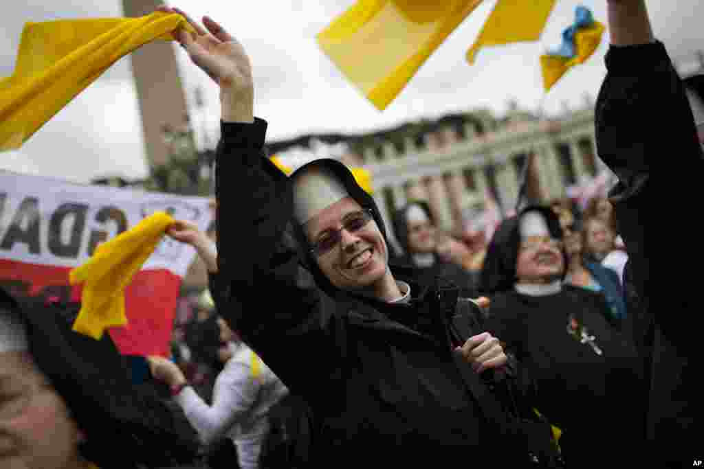 Para biarawati melambaikan tangannya pada Paus Fransiskus yang melewati kerumunan setelah memimpin upacara kanoninasi di Lapangan Santo Petrus di Vatikan, 27 April 2014.