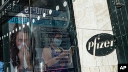 FILE - An ad for COVID-19 testing reflects on glass at a bus stop, as pedestrians walk past Pfizer world headquarters in New York, Nov. 9, 2020.