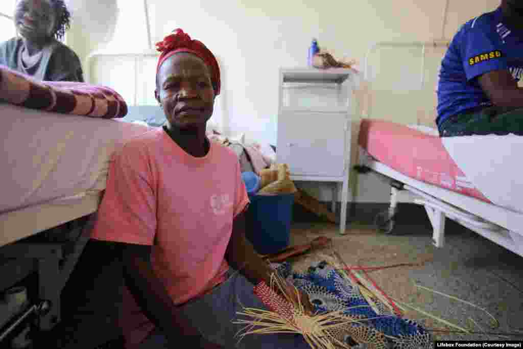 Carer sits on the floor between beds on the recovery ward, weaving.