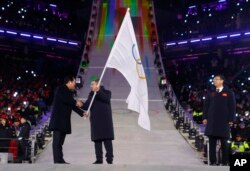 International Olympic Committee President Thomas Bach, center, receives the Olympic flag from Sim Jae-guk, left, the mayor of Pyeongchang, during the closing ceremony of the 2018 Winter Olympics in Pyeongchang, Feb. 25, 2018.