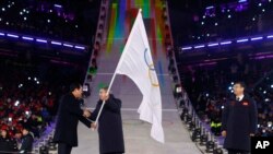 International Olympic Committee President Thomas Bach, center, receives the Olympic flag from Sim Jae-guk, left, the mayor of Pyeongchang, during the closing ceremony of the 2018 Winter Olympics in Pyeongchang, Feb. 25, 2018. 