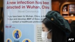 Seorang perempuan mengenakan masker melintas di depan papan pemberitahuan Kesehatan Masyarakat Inggris di Terminal 4 Bandara Heathrow di London, yang memperingatkan wabah virus corona di Wuhan, China, Selasa, 28 Januari 2020. (Foto: AFP)