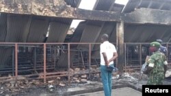A journalist, policeman and a soldier observe the damage in front of the main prison after the fire, in Gitega, Burundi, Dec. 7, 2021 