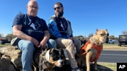 Los militares estadounidenses retirados Timothy Siebenmorgen, a la izquierda, y Mark Atkinson, a la derecha, se sientan con sus perros de servicio, Rosie y Lexi, en Kansas City, el 7 de noviembre de 2024. (AP/Nick Ingram)