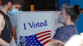 A voter fills out his ballot as a woman waits her turn during primary voting at the public safety building in McKeesport, Pa., Tuesday, June 2, 2020. (AP Photo/Gene J. Puskar)