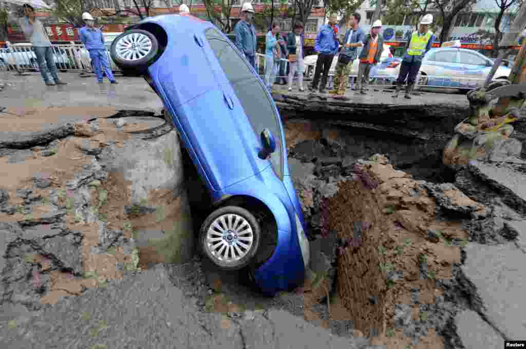 Para pekerja memperhatikan sebuah mobil yang terperosok di lubang di tengah jalan di Lanzhou, provinsi Gansu, China. Pengemudi mobil tersebut berhasil keluar tanpa terluka, menurut media setempat.