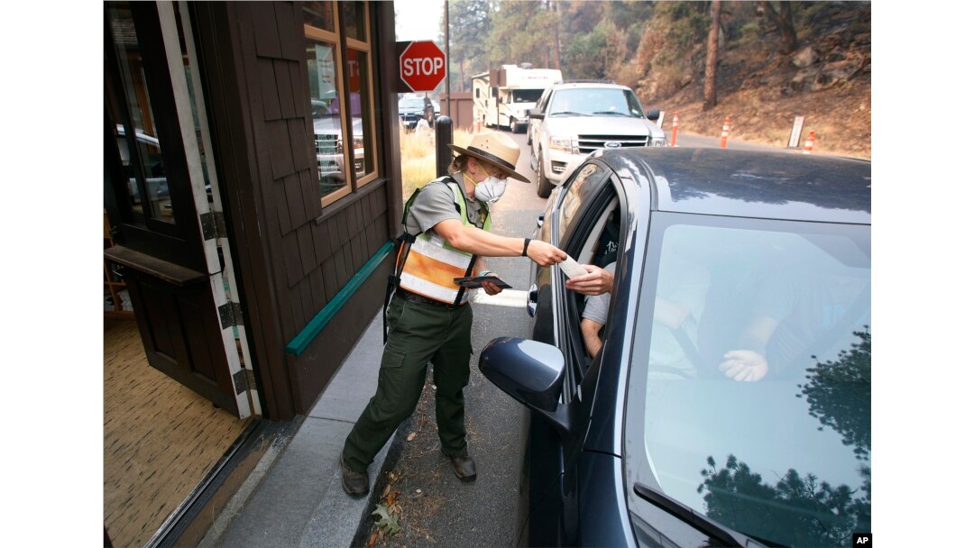 Park Ranger Anne Simmons passes maps out and directs visitors at the Hwy 140 gate as Yosemite National Park reopens after a three-week closure from smoke and fires that led to most tourists canceling their trips, Aug. 14, 2018 in Yosemite, California.