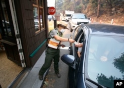 Park Ranger Anne Simmons passes maps out and directs visitors at the Hwy 140 gate as Yosemite National Park reopens after a three week closure from smoke and fires that led to most tourists canceling their trips, Aug. 14, 2018 in Yosemite, California.