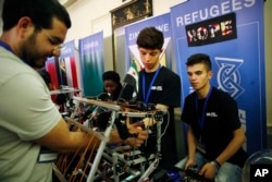 Amar Kabour, center, and Mahir Alisawaui, right, both Syrian refugees living in Lebanon, are helped with their robot by their mentor, Osama Shadeh, who is also a Syrian refugee, during the FIRST Global Robotics Challenge, July 18, 20