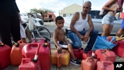Ricardo Gonzalez sits on a gas container with his uncle Miguel Colon as hundreds of people wait in line since early morning hours to buy gasoline three days after the impact of Hurricane Maria in Carolina, Puerto Rico, Sept. 23, 2017.