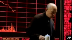 A man walks past an electronic board displaying stock prices at a brokerage house in Beijing, Monday, Jan. 11, 2016.