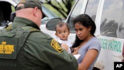 A mother migrating from Honduras holds her 1-year-old child as she surrenders to U.S. Border Patrol agents after illegally crossing the border near McAllen, Texas, June 25, 2018.