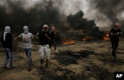 Palestinian protesters run for cover from tear gas fired by Israeli troops after they burn tires during a protest at the Gaza Strip's border with Israel, east of Khan Younis, May 4, 2018.