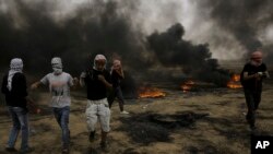 Palestinian protesters run for cover from tear gas fired by Israeli troops after they burn tires during a protest at the Gaza Strip's border with Israel, east of Khan Younis, May 4, 2018. 