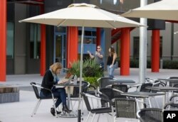 In this photo taken Feb. 3, 2015, a woman works on her laptop as two other women walk through the campus at Facebook headquarters in Menlo Park, Calif.