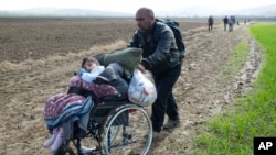 Un migrant venant d'Irak pousse le fauteuil roulant de sa fille handicapée de 8 ans pour arriver à la frontière grecque d'Idomeni, mardi 1er Mars 2016. (AP Photo/Petros Giannakouris)