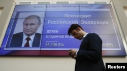 A man walks past a screen showing preliminary results of Russian President Vladimir Putin in the presidential election, at the headquarters of Russia's Central Election Commission in Moscow, March 19, 2018. 