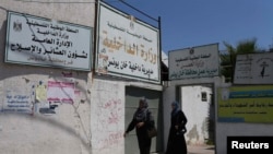 Palestinian Women walk past the closed office of the Ministry of Interior in Khan Younis in the southern Gaza Strip, June 26, 2014. 