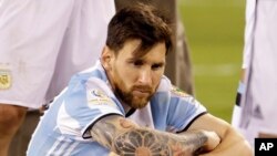 Déçu et assis sur la pelouse, Lionel Messi de l'Argentine attend la remise des médailles et du trophée après la défaite de la sélection argentine 2-4 face à celle du Chili lors de la Copa America Centenario, à East Rutherford, N.J., 26 juin 2016.