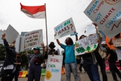 Pemuda-pemuda yang membawa plakat dan bendera merah putih mengikuti aksi unjuk rasa saat Asia Climate Rally, di luar Monumen Nasional (Monas) di Jakarta, 27 November 2020. (Foto: REUTERS/Willy Kurniawan)