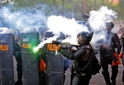 Seorang polisi menembakkan gas air mata saat bentrok dengan para mahasiswa yang berunjuk rasa di Surabaya, Jawa Timur, 8 Oktober 2020. (Foto: AP)