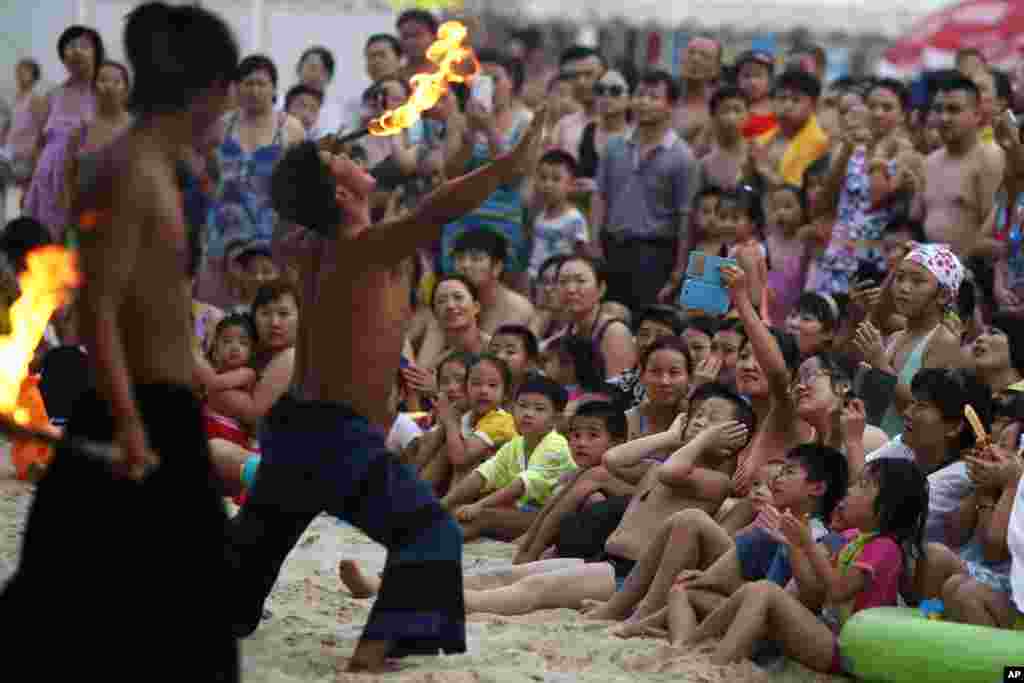 A performer places a burning stick to his tongue during a show for visitors to a beach carnival in Beijing, China.