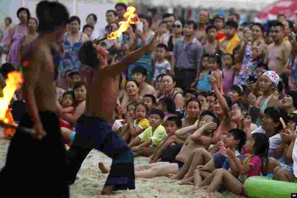 A performer places a burning stick to his tongue during a show for visitors to a beach carnival in Beijing.