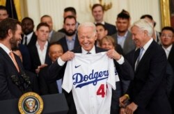El presidente Joe Biden recibe una camisa de los Dodgers en la bienvenida que les ofreció el 2 de julio en la Casa Blanca, a su derecha el pitcher Clayton Kershaw y a la izquierda el dueño del equipo, Mark Walter.
