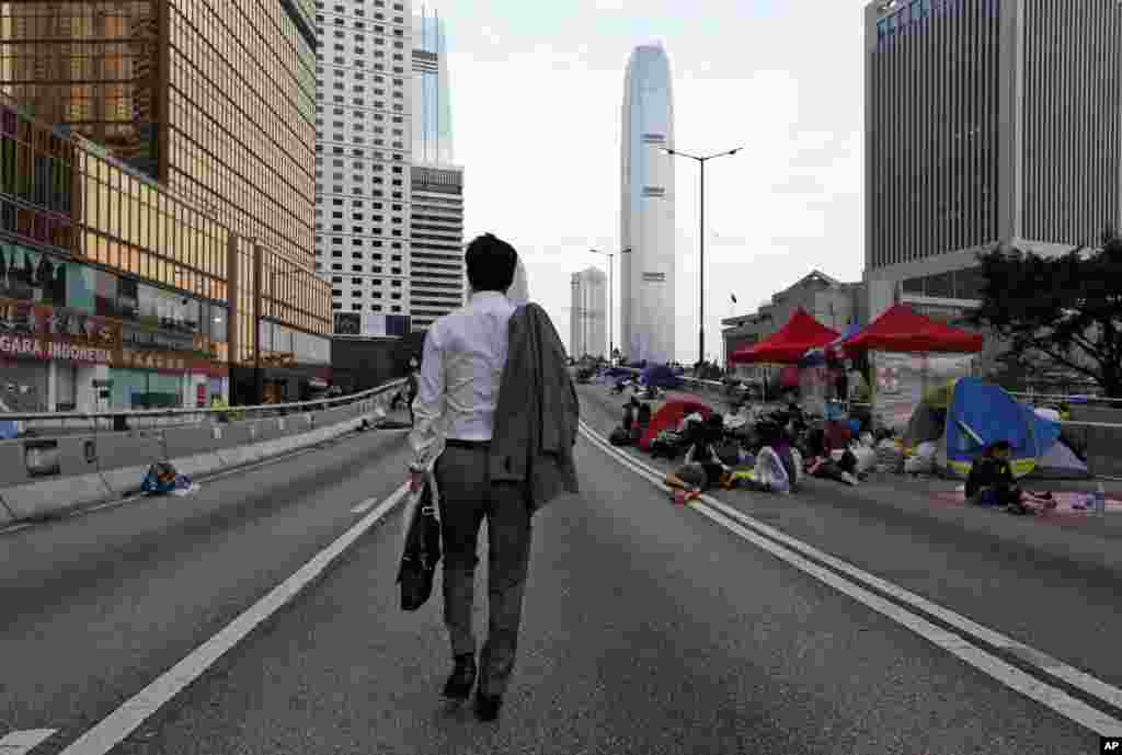 A man walks to work as the pro-democracy student protesters sleep on a roadside in the occupied areas surrounding the government complex in Hong Kong, Oct. 6, 2014. 