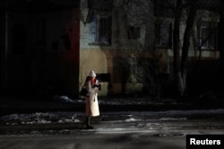 A woman is lit by a passing car as she stands in a dark street during partial power cuts following a Russian attack on Ukrainian energy facilities, amid Russia's attack on Ukraine, in central Kyiv, Ukraine, Dec. 13, 2024.