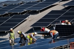 FILE - In this Aug. 8, 2019, photo, workers install solar panels at the Van Nuys Airport in Los Angeles.