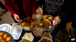 Para tamu menambahkan guacamole dan pico de gallo ke latkes selama acara Chicanukah di Holocaust Museum Houston, di Houston, Texas, 19 Desember 2024.