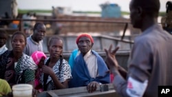 FILE - A worker with a non-governmental organization (NGO) explains to recently-arrived displaced people where they can find some of the limited services available to them, in a village in Awerial, South Sudan, Jan. 16, 2014.