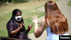 Le directeur de Empowering Deaf Society, Mangai Sutharsan (avec un masque partiellement transparent), parle en langue des signes avec l'interprète Leanne Barsdell à Ilford, Londres, Grande-Bretagne, le 29 juillet 2020. Photo prise le 29 juillet 2020. . REUTERS / Hannah McKay