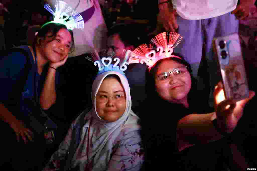 Women wearing '2025' head bands take a selfie pictures during the New Year's Eve celebrations in Jakarta, Indonesia, Dec. 31, 2024.