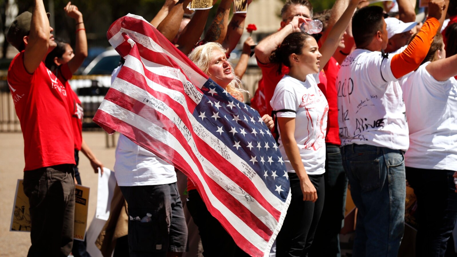FILE - A woman holds up a U.S. flag as she other anti-deportation protesters chant in front of the White House in Washington.