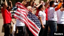 FILE - A woman holds up a U.S. flag as she other anti-deportation protesters chant in front of the White House in Washington.