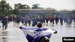 Un migrante, parte de una caravana que viaja a Estados Unidos, sostiene una bandera hondureña mientras cruza el río Suchiate en la frontera entre Guatemala y México, en Ciudad Hidalgo, México, el 20 de enero de 2020.