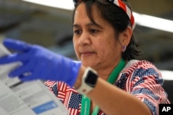 A woman wears an American flag headband, earrings and shirt while opening ballots to prepare for counting at King County Elections headquarters on Election Day, Nov. 5, 2024, in Renton, Washington.