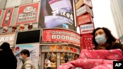 Residents wearing masks past by a screen showing a trailer for the film "Days and Nights in Wuhan" outside a mall in Wuhan in central China's Hubei province on Friday, Jan. 22, 2021. China is rolling out the state-backed film praising Wuhan ahead of…