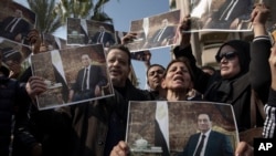 Supporters of ousted President Hosni Mubarak hold posters with his photograph near the cemetery where he will be buried, in the Heliopolis neighborhood of Cairo, Egypt, Feb. 26, 2020.