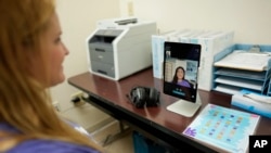 FILE - Therapist Norma Kawatta, seen on screen, talks to Paris Carroll, VP of mental health clinical services for Hazel Health, as the pair demonstrate how the company's telehealth therapy service works on World Mental Health Day, Tuesday, Oct. 10, 2023,